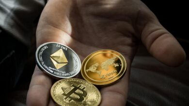 Hand holding Bitcoin, Ethereum, and Ripple coins representing digital currency.