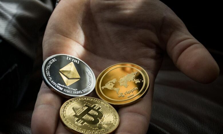 Hand holding Bitcoin, Ethereum, and Ripple coins representing digital currency.