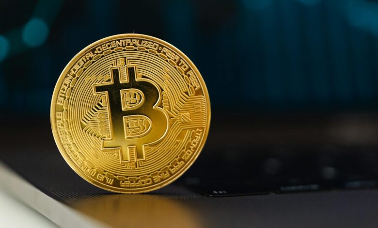 Golden Bitcoin coin standing upright on a laptop keyboard, representing digital currency.