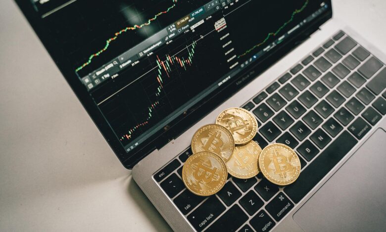 Golden bitcoin coins placed on a laptop keyboard with trading chart displayed on the screen.