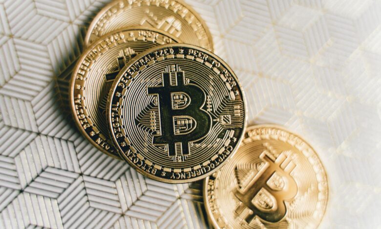 A close-up image of gold Bitcoin cryptocurrency coins on a geometric patterned surface.