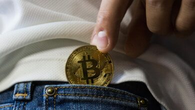 Close-up of hand putting Bitcoin in jeans pocket symbolizing cryptocurrency savings.